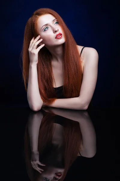 Young woman with ginger hair over reflection mirror on blue back