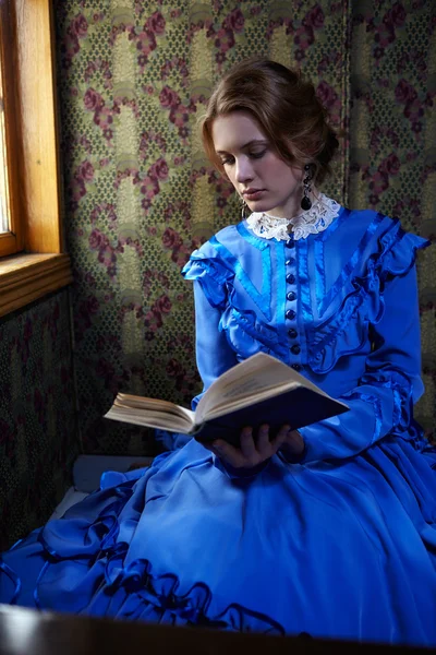 Young woman in blue vintage dress reading the book in coupe of r
