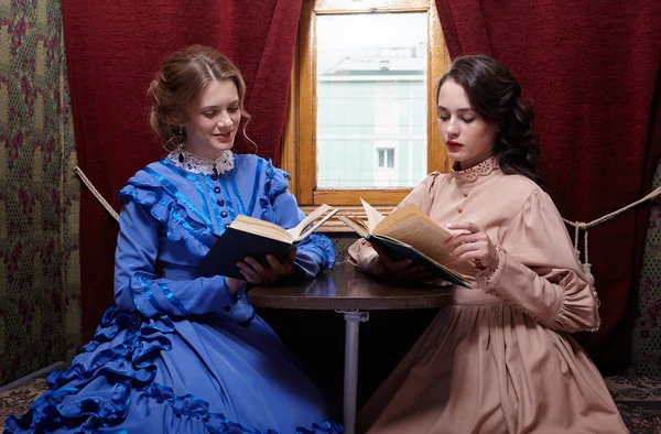 Two sisters in retro dress reading books in train compartment