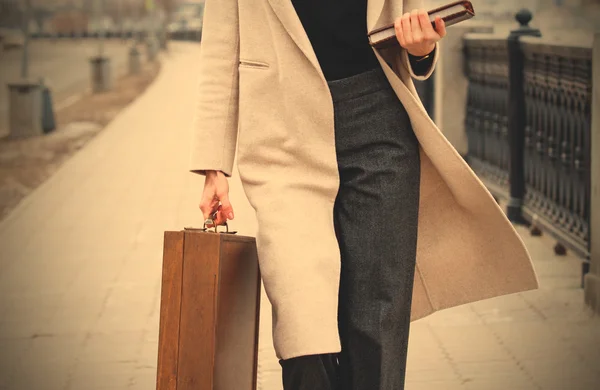 Woman in a light coat, with a wooden case