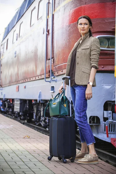 Beautiful middle-aged woman with luggage near retro train