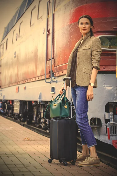 Beautiful middle-aged woman with luggage near retro train