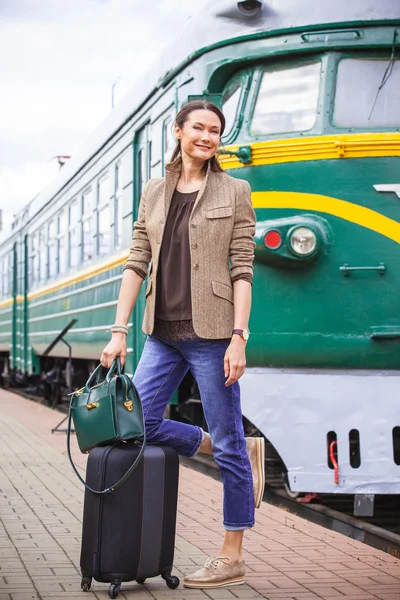 Smiling middle-aged woman with luggage near old train