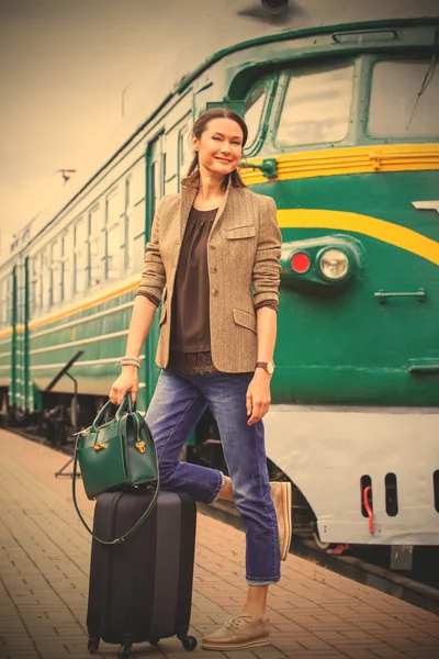 Smiling middle-aged woman with luggage near old train