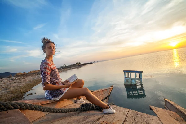 Young woman is sitting on the shipwreck and reading a book.