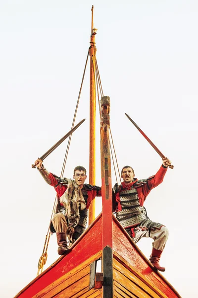 Two warriors in armor with the swords on the bow of a sailing sh