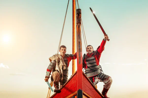 Two warriors in armor with the swords on the bow of a sailing sh