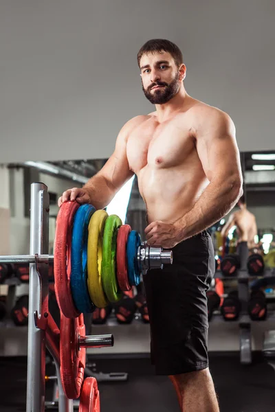 Powerful man with muscular build is standing near the barbell in