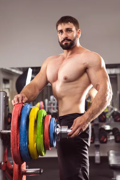 Powerful man with muscular build is standing near the barbell in