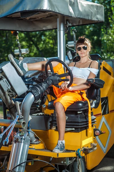Sexy woman in orange overalls is operating the tractor.