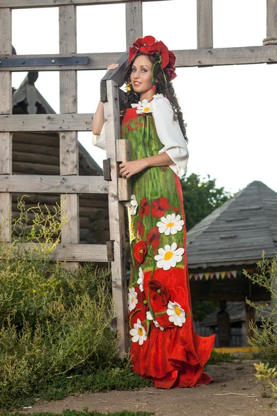 Young woman in Russian traditional dress is standing near wooden