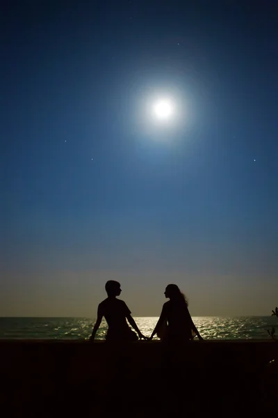 Yong couple is sitting under the moon and stars on the tropical