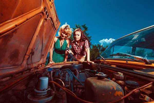 Beautiful woman mecanic is repairing a car another woman is watc