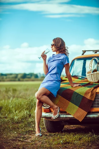 Beautiful woman on the picnic is drinking wine near a car.