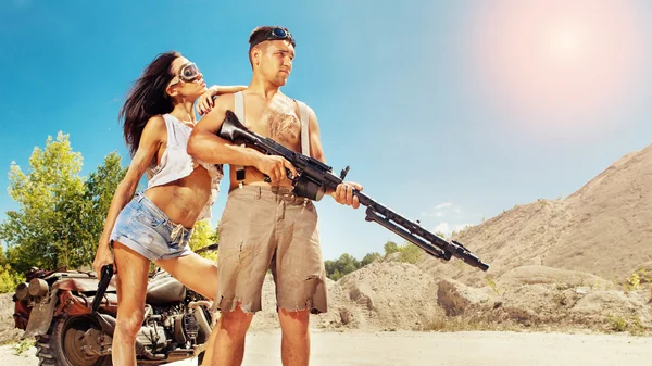 Sexy couple of bikers with guns on the desert background.