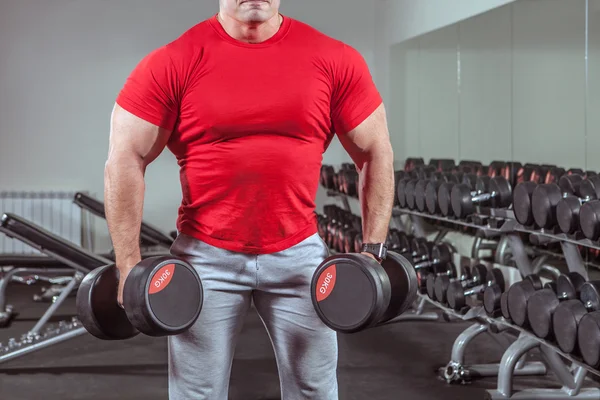 Powerful man with muscular build is training with the dumbbells