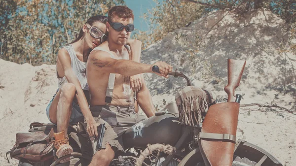 Sexy couple of bikers with guns on the summer background.