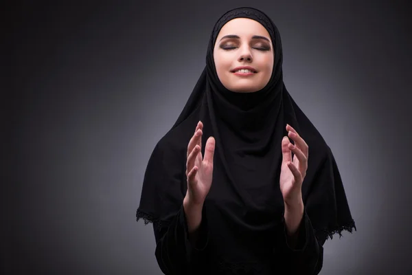 Muslim woman in black dress against dark background