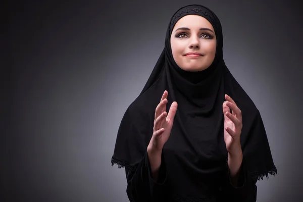 Muslim woman in black dress against dark background
