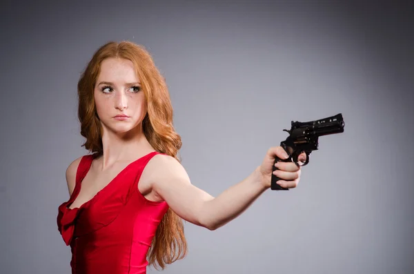 Pretty young girl in red dress with gun isolated on grey