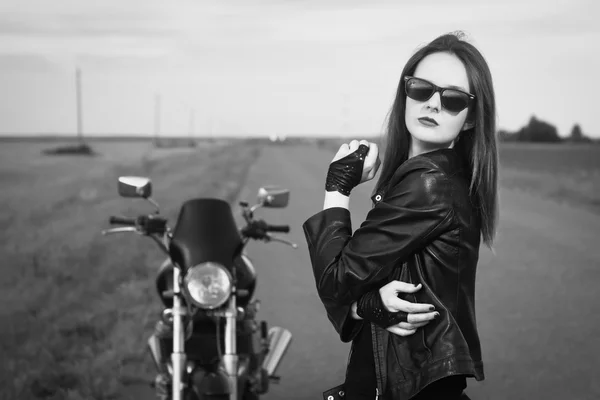 Biker girl in a leather jacket posing near motorcycle