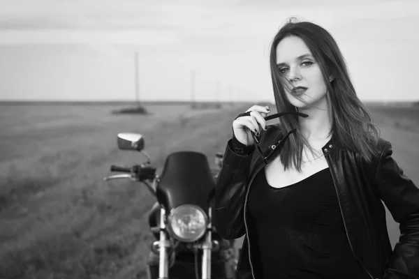 Biker girl in a leather jacket posing near motorcycle