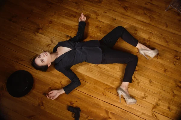 Woman in a black suit with gun lying on the floor