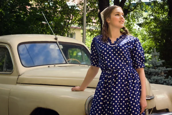 Lady in vintage dress standing near retro car
