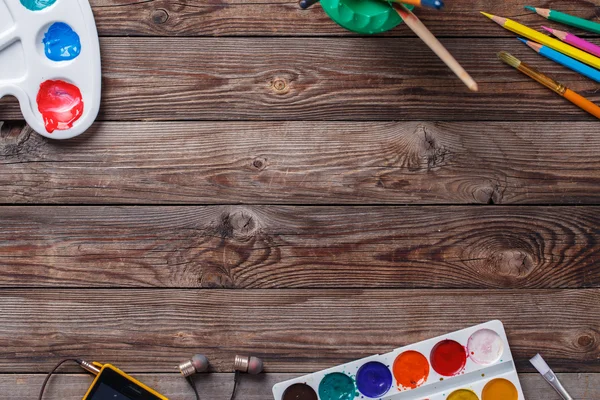 Paper, watercolors, paint brush and some art stuff on wooden   table