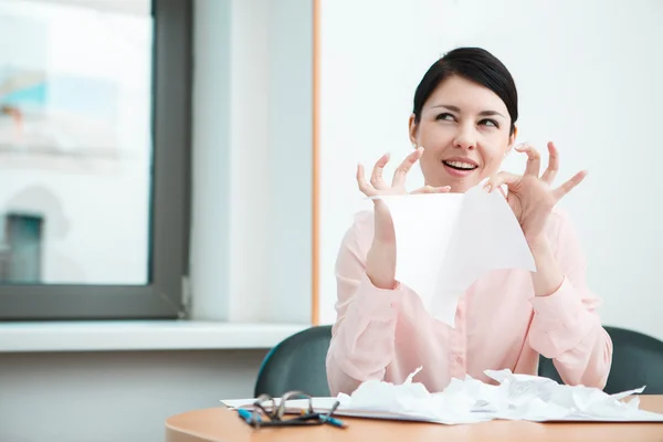 Business woman sitting her desk getting rid of old papers with pleasure.