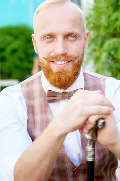 Smiling blonde guy in bow tie and cane in hands