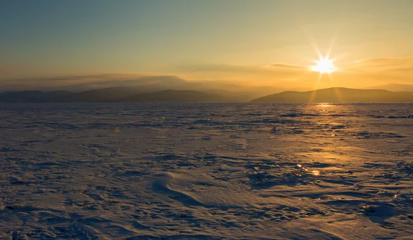 Rays of rising sun light up the snow covered ice.