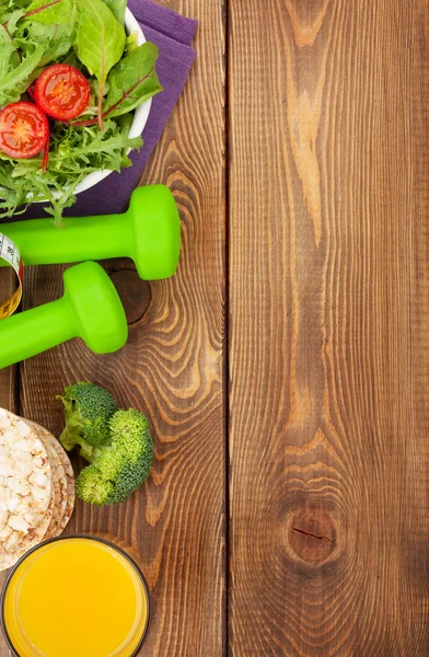 Dumbells, tape measure and healthy food over wooden background