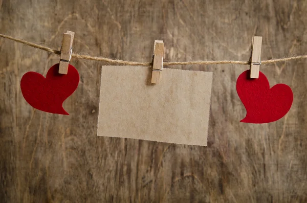 Two Red fabric hearts with sheet of paper hanging on the clothes