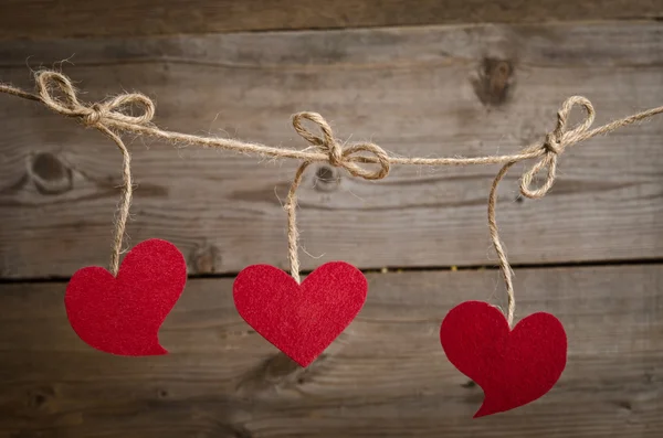 Three Red fabric hearts hanging on the clothesline . On old wood