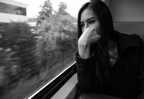 Portrait of beautiful young woman with long hairs looks out of train window.