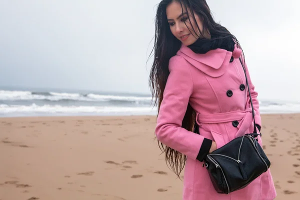 Portrait of attractive young woman with long beautiful hairs dressed pink coat, which posing in autumn North sea beach.