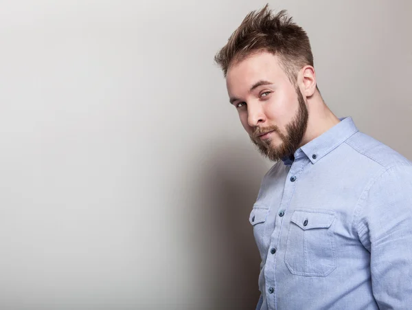 Portrait of young handsome friendly man in blue shirt. Studio photo on light grey background.