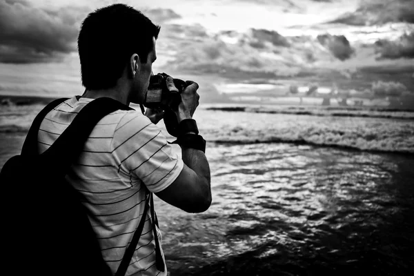 Photographer traveler photographs a sunset over ocean. Black-white photo with copy-space.