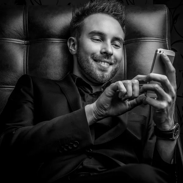 Handsome young man in dark suit relaxing on luxury sofa. Black-white photo.
