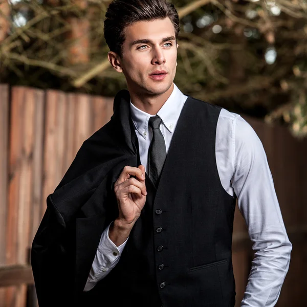 Elegant handsome man in classical suit poses near wooden fence