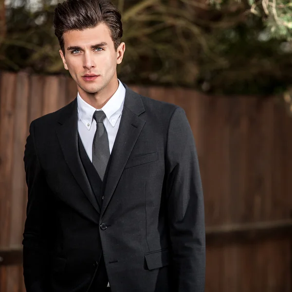 Elegant handsome man in classical suit poses near wooden fence