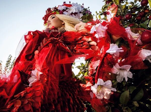 Fashion image of sensual girl in bright red fantasy stylization. Outdoor fairy tale art photo.