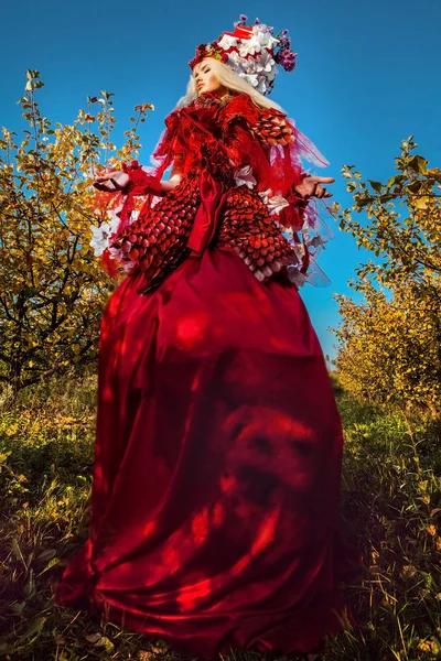 Fashion image of sensual girl in bright red fantasy stylization. Outdoor fairy tale art photo.