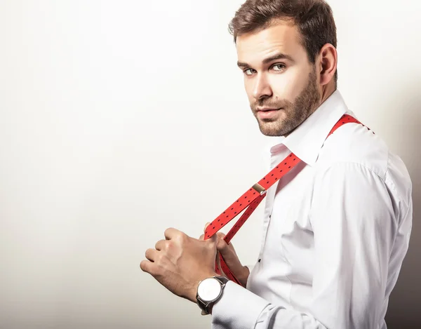 Elegant young handsome man in white shirt with red braces. Studio fashion portrait.
