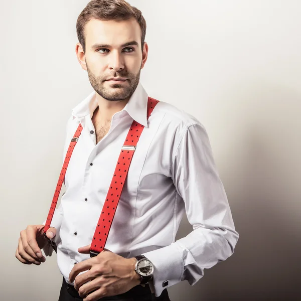 Elegant young handsome man in white shirt with red braces. Studio fashion portrait.