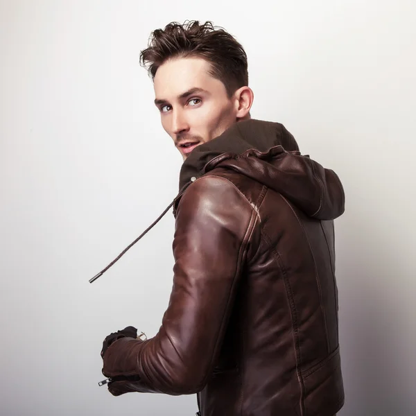 Attractive young man in a brown leather jacket pose in studio.