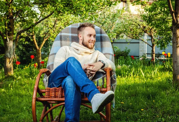 Handsome man relax in rocking-chair with plaid in a summer garden.