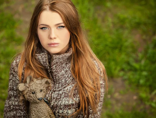 Young attractive girl in a brown sweater poses on park with bear figurine.