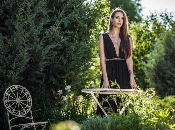 Outdoors portrait of beautiful young woman in luxury black dress posing in summer garden.